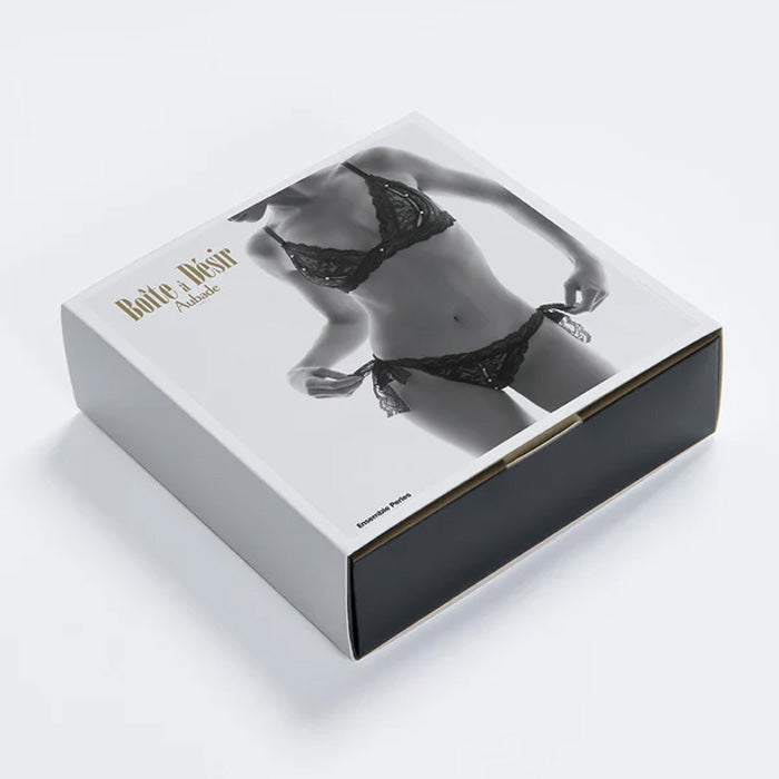 Geschenkbox mit dem schwarzen Lingerie-Set ouvert aus Spitze mit Perlen und offenem Triangel-BH und offenem Tanga-Slip von Aubade Paris
